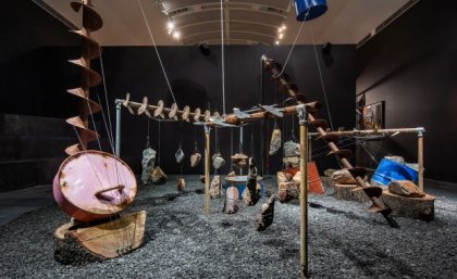 A room with dark walls is filled with an art installation of industrial mining equipment repurposed into musical instruments.